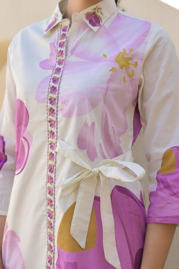 Woman wearing a white and lavender floral print 2-piece co-ord set with a side-tie tunic and straight pants.